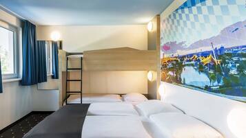 A hotel room with a bunk bed, a desk, a window with curtains, and a wall-mounted artwork.