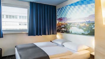 A hotel room with a bed, a desk, a window with curtains, and a wall with a cityscape mural.