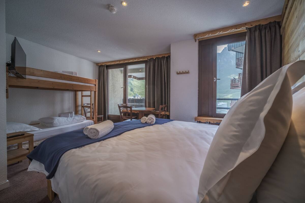A hotel room with a bunk bed, a desk, and a view of mountains.