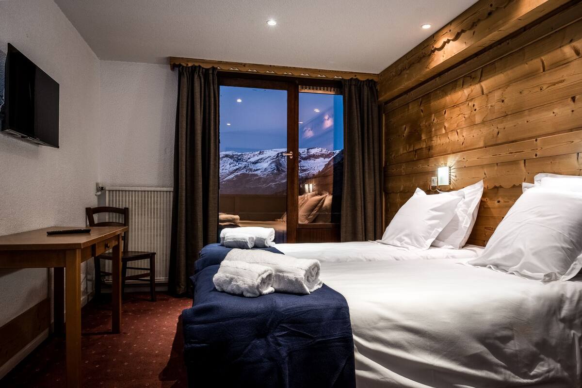 A hotel room with a bed, a desk, and a view of a snowy mountain landscape through a window.