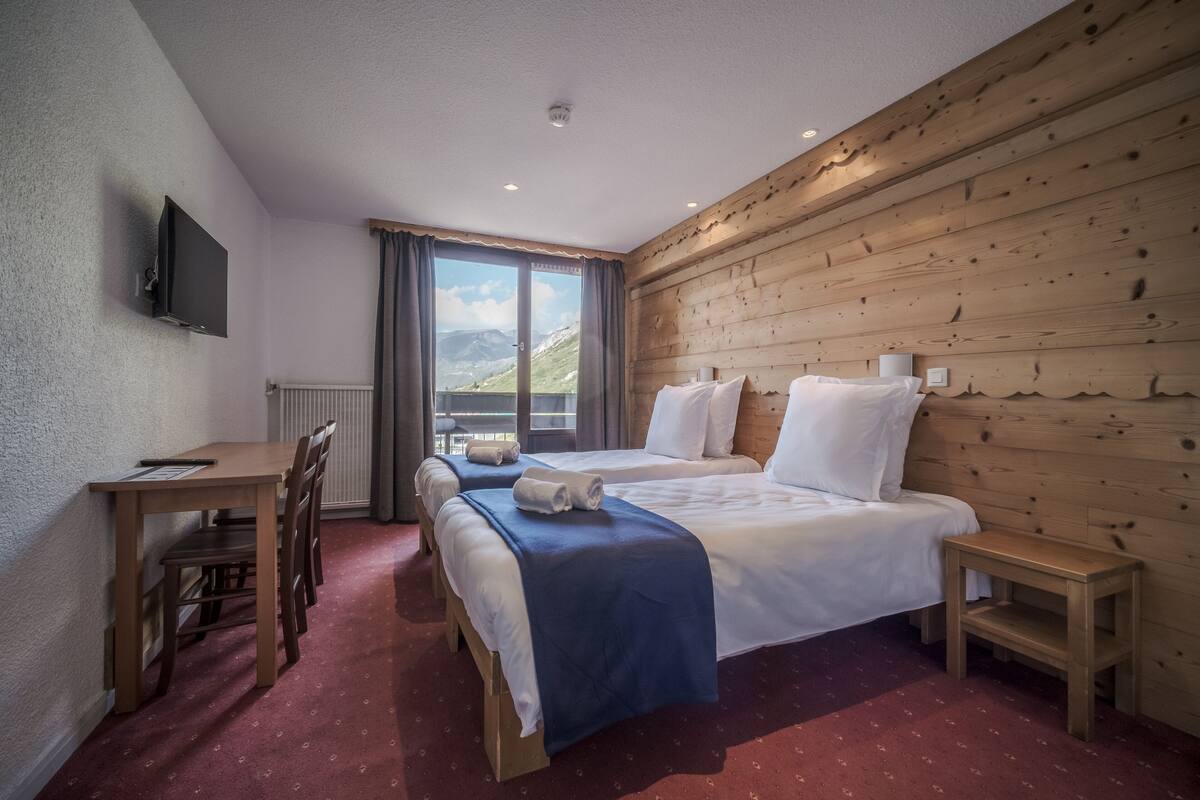 A hotel room with two beds, a desk, and a TV.