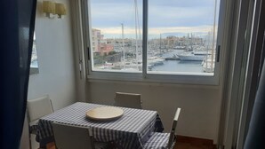 Un comedor con mesa y sillas, vista a un puerto deportivo con barcos, y un paisaje urbano al fondo.