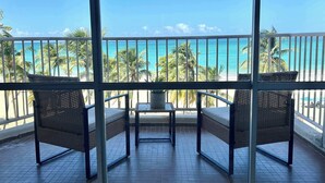 Un balcon doté de meubles en osier, d’un sol carrelé et offrant une vue sur la plage et l’océan.