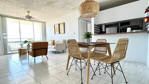 Un vaste espace de vie comprenant une table à manger, des chaises en osier, un canapé et un ventilateur de plafond.