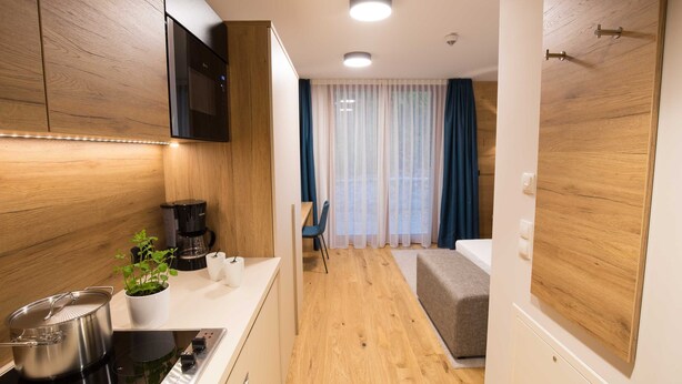 Una cocina moderna con armarios de madera, un microondas empotrado y una estufa. Hay una zona de comedor con una mesa y sillas, y un sofá al fondo.