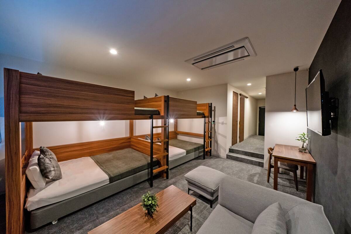 A modern room with bunk beds, a sofa, a small table with a plant, and a TV mounted on the wall.