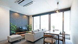 Una sala de estar moderna con sofá, reposapiés, mesa de comedor, sillas y un televisor de pantalla plana.