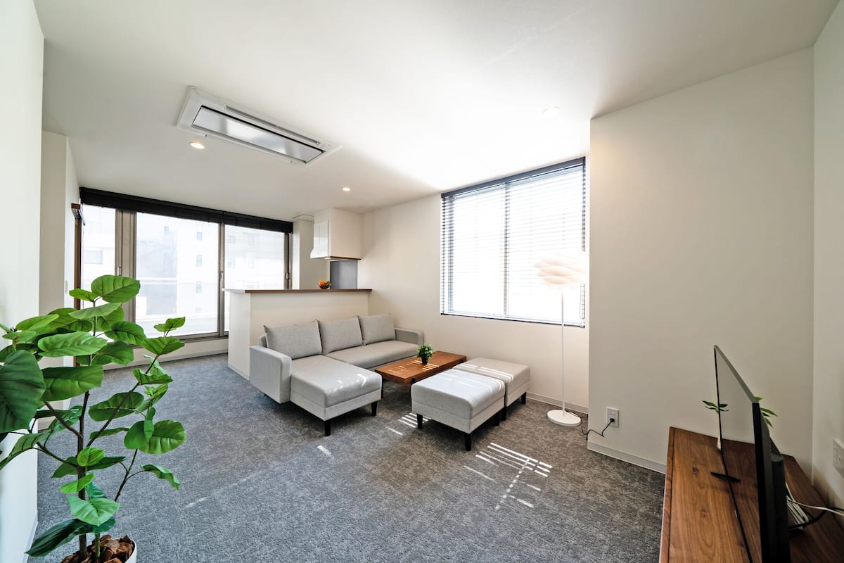 A modern living room with a grey sofa, a wooden coffee table, and a TV on a wooden stand.