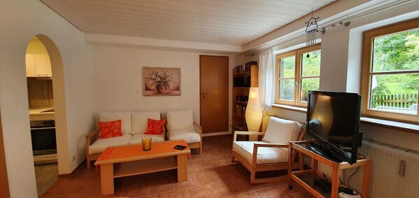 A cozy living room with a sofa, armchairs, a coffee table, a TV, and a bookshelf.