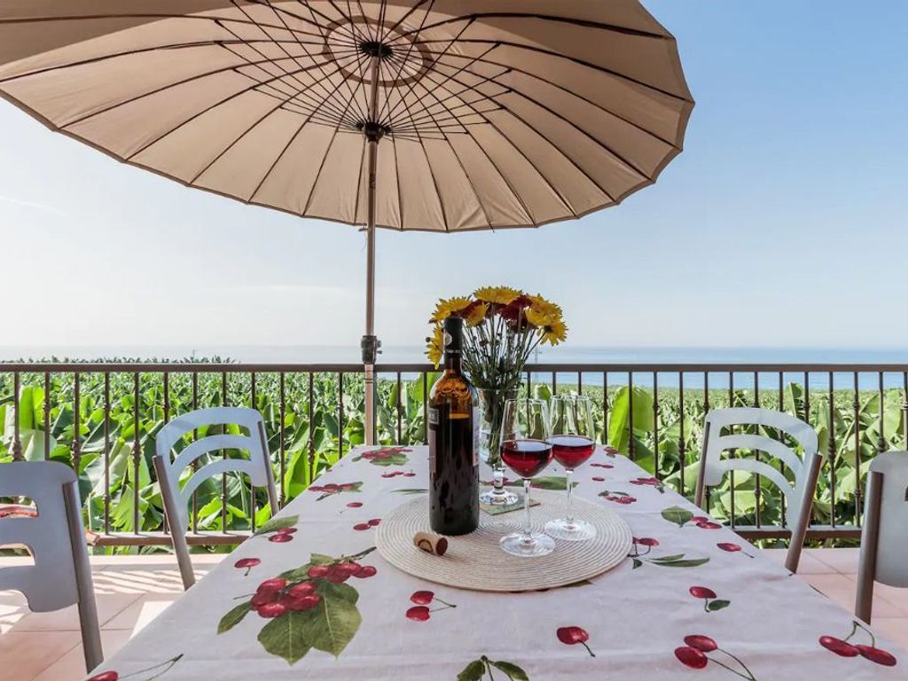 Une table dressée à l’extérieur, avec une nappe, une bouteille, des verres et un parasol.