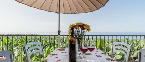 Une table dressée à l’extérieur, avec une nappe, une bouteille, des verres et un parasol.
