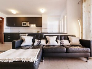 Ein modernes Wohnzimmer mit einem schwarzen Ledersofa, einer weißen Decke und einer Küche im Hintergrund.