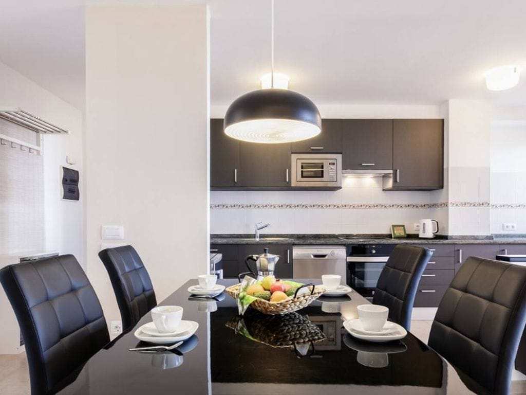 A modern kitchen with dark cabinetry, a central island, and a dining area with black chairs and a black table.