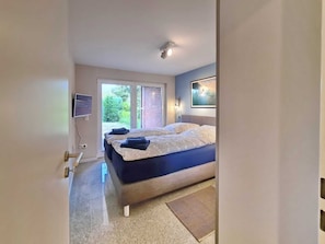 Un dormitorio con una cama grande, un televisor montado en la pared y un ventanal corredero que da a un jardín.