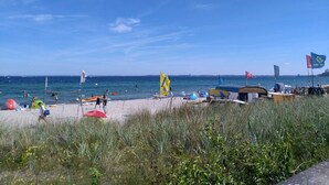 A beach with tents, flags, and people. - Malibu SA 57a - Malibu, 3 rooms, 65m², terrace, sauna (Scharbeutz)