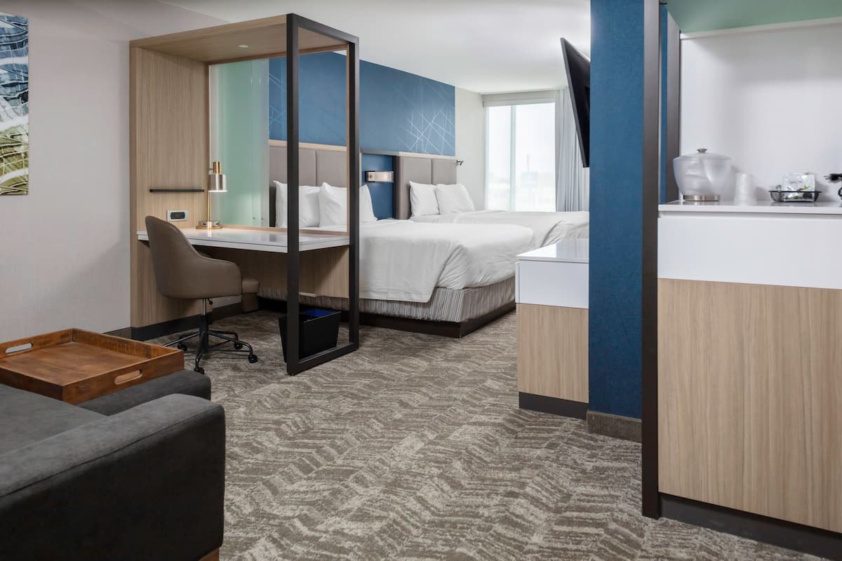 A hotel room with a desk, two beds, a seating area, and a kitchenette.