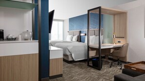 Habitación de hotel con cama, escritorio, silla, cafetera y televisor.