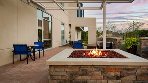 Un patio con una chimenea de piedra, sillas azules y una puerta de cristal que da a un edificio.