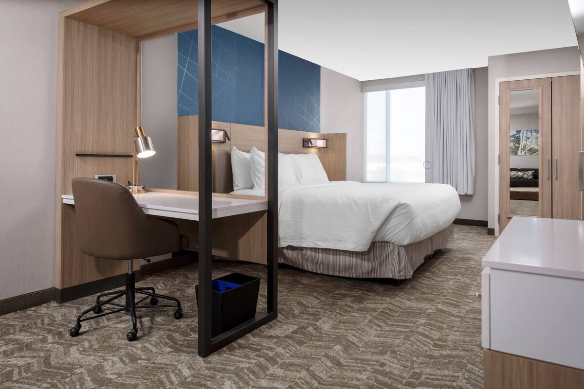 A hotel room with a bed, desk, chair, and a wardrobe.