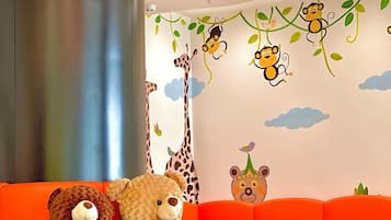 Zona de juegos infantiles con sofá, dos osos de peluche y adornos de pared con animales y pájaros.