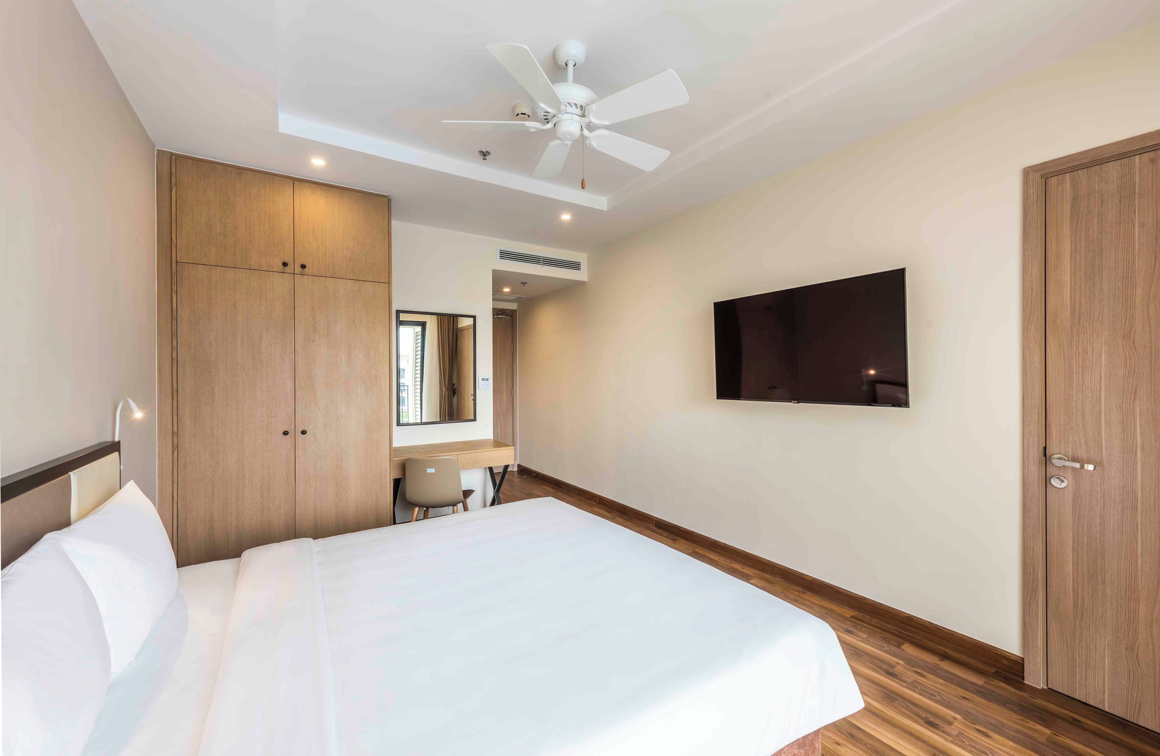 Une chambre d’hôtel équipée d’un lit, d’un bureau, d’une armoire, d’un ventilateur de plafond et d’un téléviseur fixé au mur.