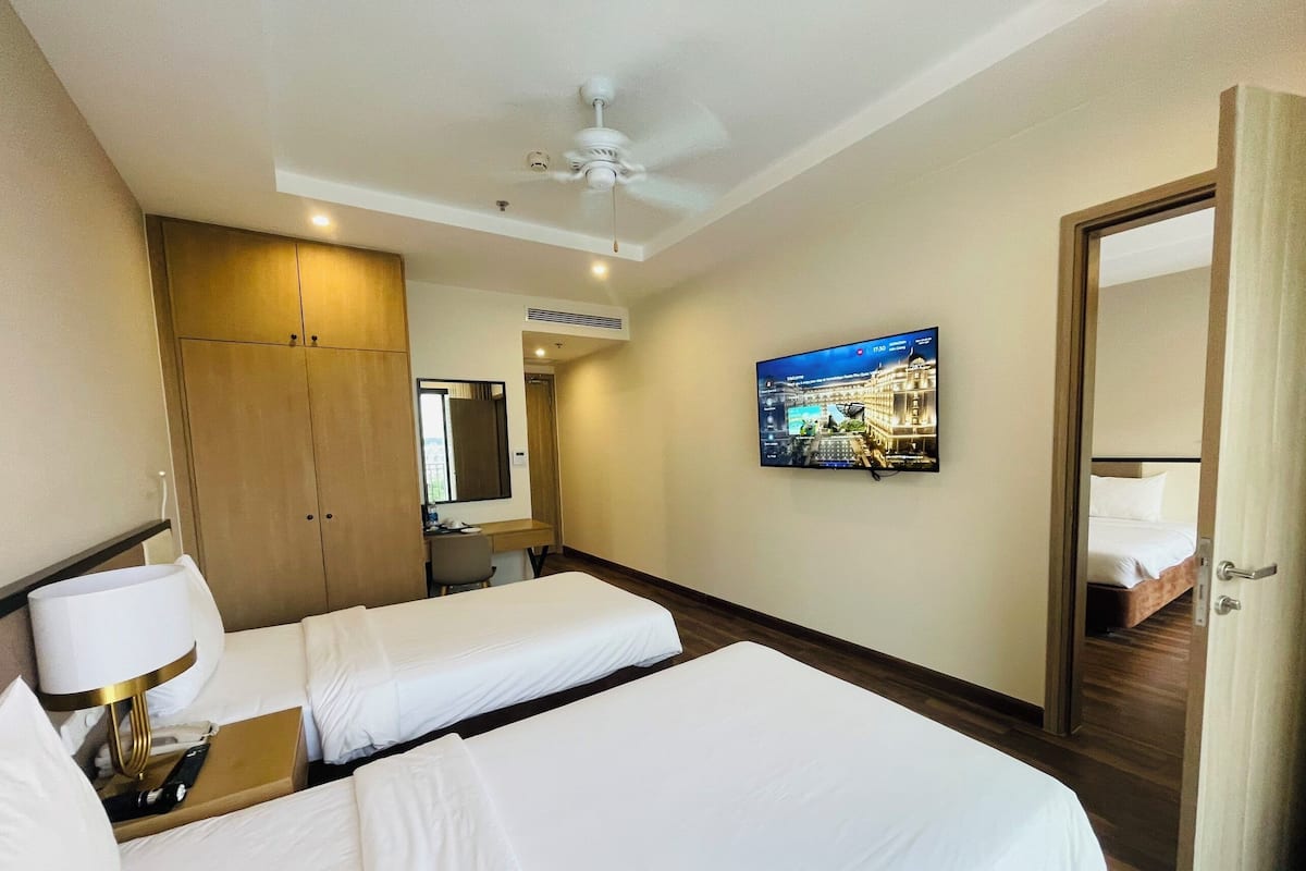 A hotel room with two beds, a desk, a mirror, a TV, and a wardrobe.