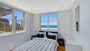 Een slaapkamer met een bed, twee nachtkastjes, een raam met uitzicht op de oceaan en een ingelijst kunstwerk aan de muur.