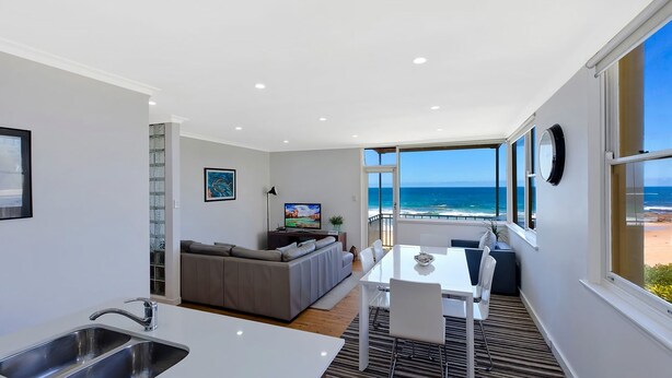 Een moderne woonruimte met een keuken, eethoek en een balkon met uitzicht op zee.