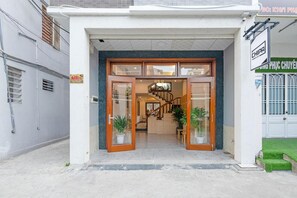 A building entrance with a staircase leading to an upper floor, potted plants, and a sign indicating the property name.