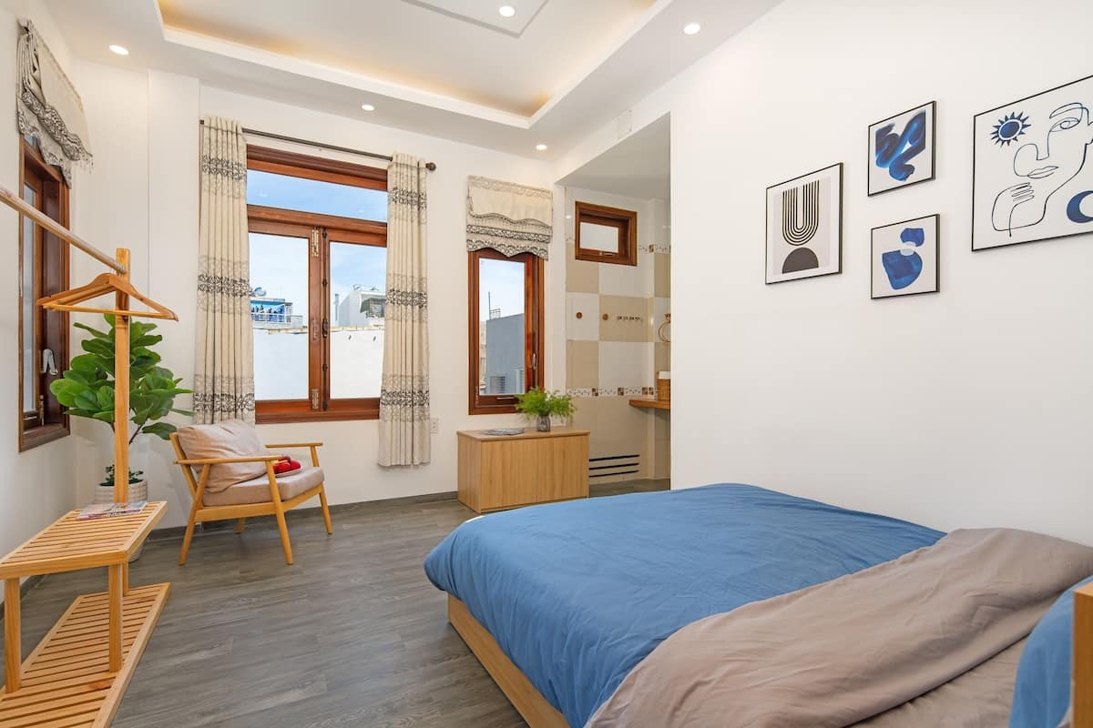 A modern bedroom with a large bed, a wooden chair, a small table, and a potted plant.