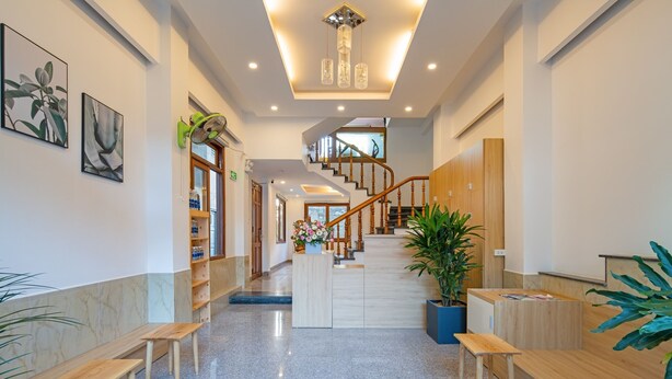 A spacious lobby with a marble floor, wooden benches, a staircase, and a reception desk. - Chipa Homestay (Da Nang)