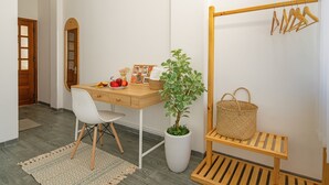 A room with a wooden desk, a white chair, a potted plant, a wooden hanger rack, and a woven basket. - Chipa Homestay (Da Nang)