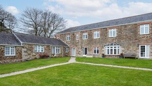 A stone building with a central courtyard, multiple windows, and a grassy lawn. - 2 Bedroom Cottage Close to Perranporth Beach (Perranzabuloe)