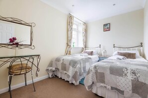 A bedroom with two beds, a desk, a chair, a mirror, and a window with curtains. - 2 Bedroom Cottage Close to Perranporth Beach (Perranzabuloe)