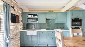 A kitchen with teal cabinets, a stone wall, and a wooden table. - 2 Bedroom Cottage Close to Perranporth Beach (Perranzabuloe)