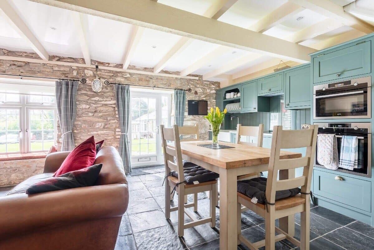 A cozy living room with a stone wall, a wooden dining table, and a leather sofa.