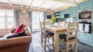 A cozy living room with a stone wall, a wooden dining table, and a leather sofa. - 2 Bedroom Cottage Close to Perranporth Beach (Perranzabuloe)