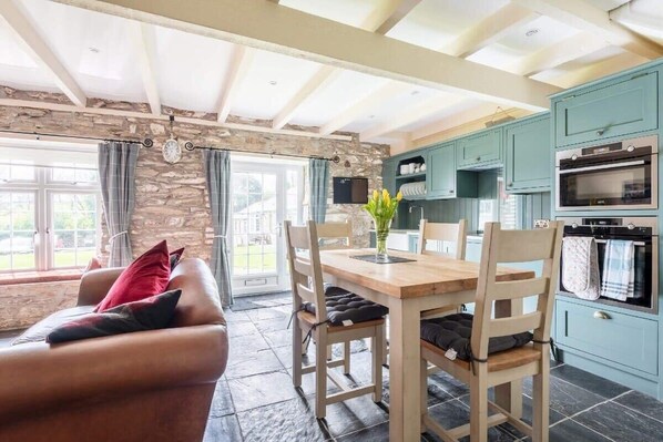 A cozy living room with a stone wall, a wooden dining table, and a leather sofa.