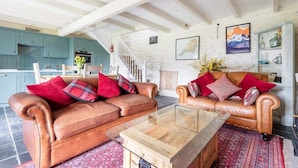 A spacious living area with two leather sofas, a glass coffee table, and a staircase leading to an upper level. - 2 Bedroom Cottage Close to Perranporth Beach (Perranzabuloe)
