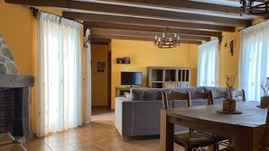A cozy living room with a fireplace, a sofa, a dining table, and a TV. - RURAL HOUSE LA CABEZUELA (El Real de San Vicente)