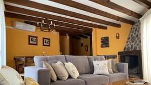 A living room with a grey sofa, wooden beams, a fireplace, and a stone wall. - RURAL HOUSE LA CABEZUELA (El Real de San Vicente)