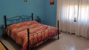 A bedroom with a bed, curtains, and a tiled floor.