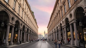 Une large rue bordée de bâtiments classiques dotés d’arcs et de colonnes, qui mène à une église imposante surmontée d’un clocher.