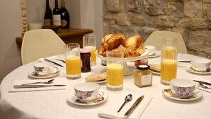 A breakfast table set with croissants, juice, and a bottle of red wine.