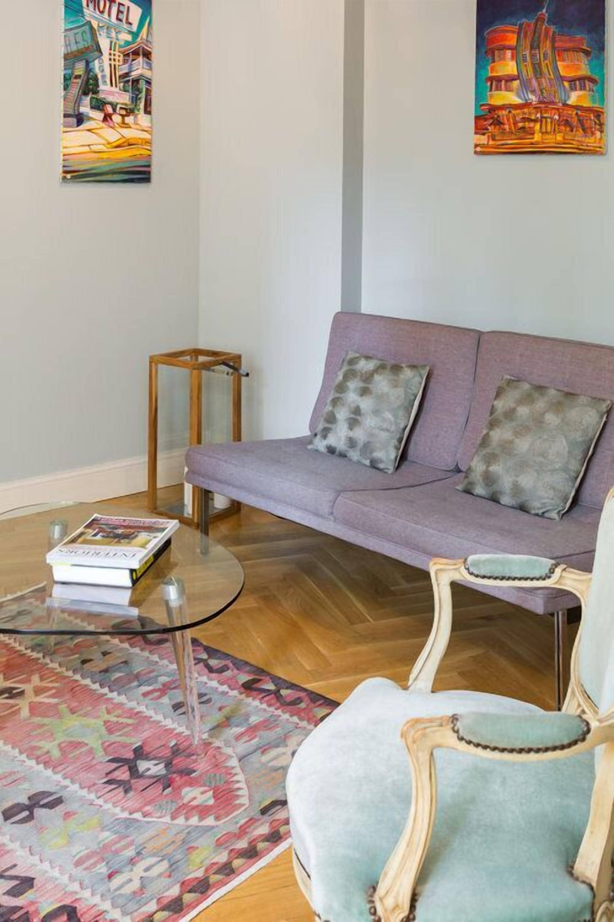 Ein Wohnzimmer mit einem violetten Sofa, einem gemusterten Teppich, einem Holztisch und zwei Wandbildern.