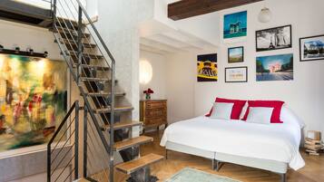 A bedroom with a bed, a staircase, and a wall with framed pictures.