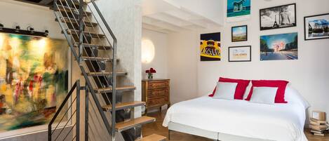 A bedroom with a bed, a staircase, and a wall with framed pictures.
