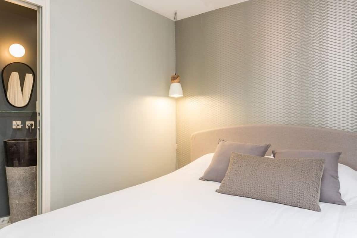 Un dormitorio con cama, almohadas, una mesita de noche, una lámpara y una pared con textura.