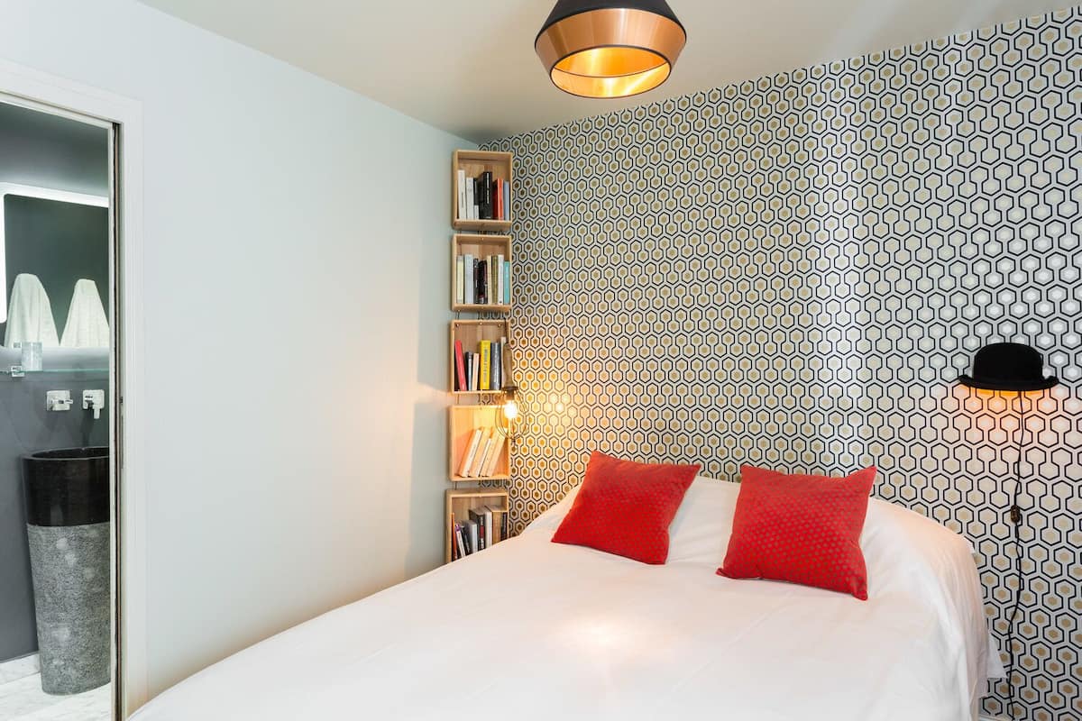 Un dormitorio con cama, estantería, lámpara de pared y pared con diseño.