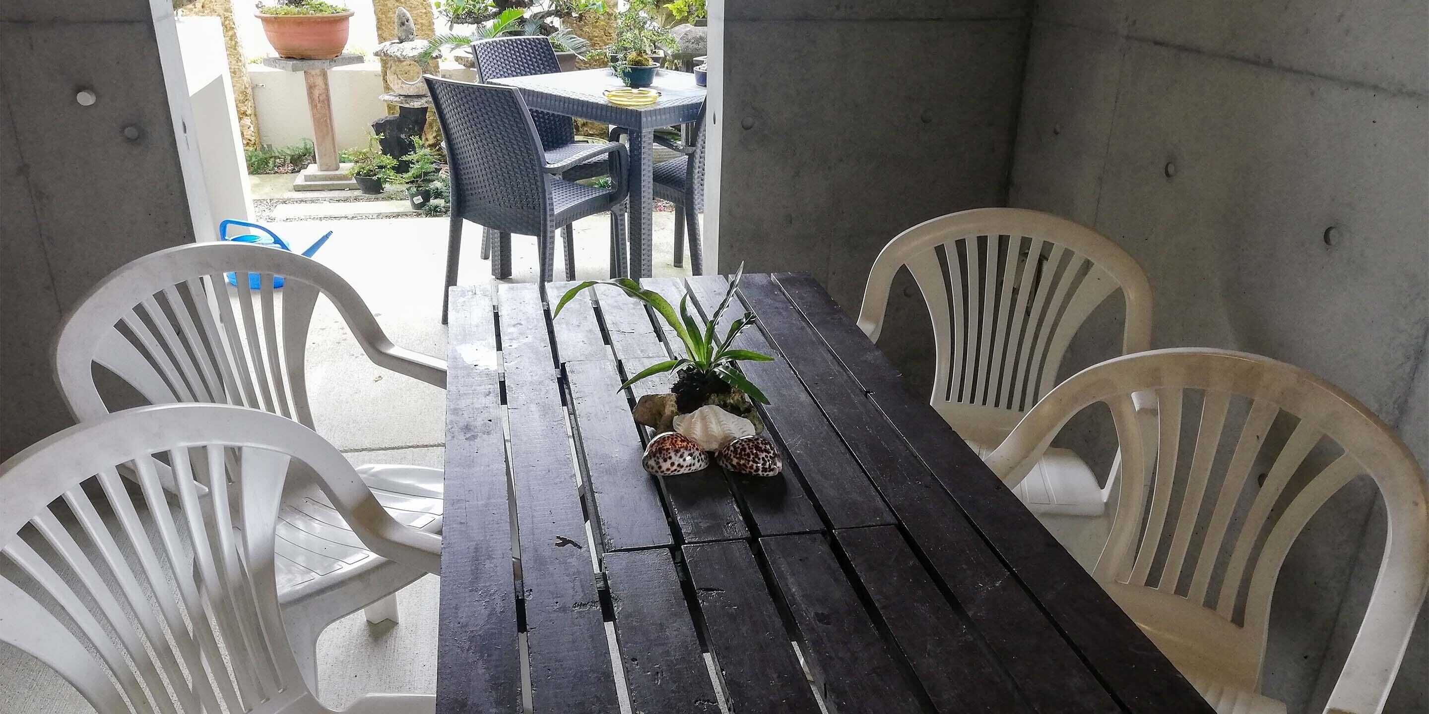 Een houten tafel met vier witte plastic stoelen, een potplant en een decoratieve schelp op de tafel.